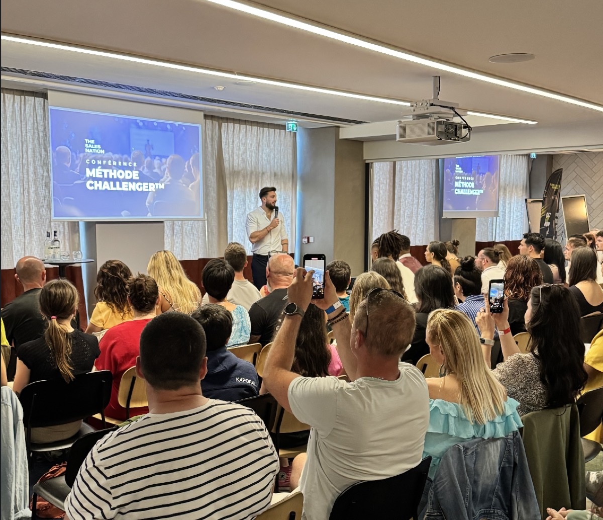 Une salle comble pendant une conférence de Julien, des participants filment.